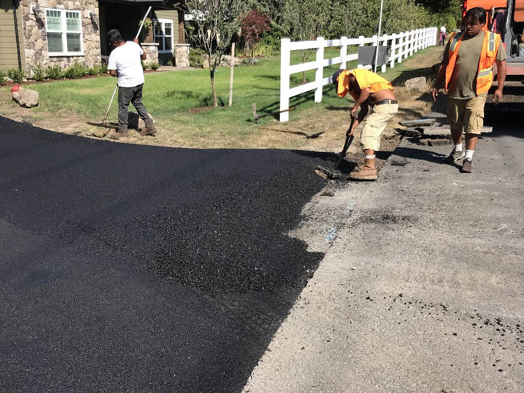 Crew raking and finishing the edge of a new asphalt driveway