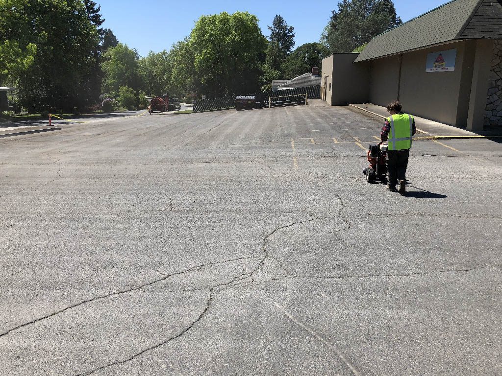 A worker sizing up a cracked driveway/parking area near a building to help illustrate Asphalt Crack Repair