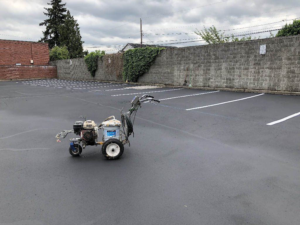 Striping machine standing on a fresh asphalt parking lot and new lines to help illustrate asphalt vs concrete