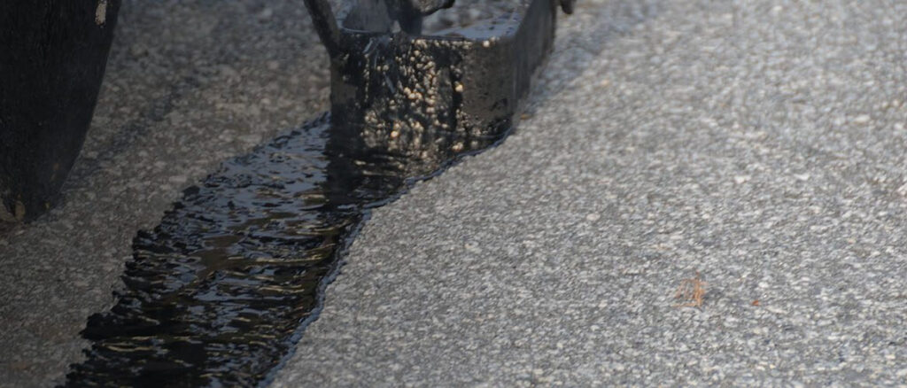 Closeup of fixing an asphalt driveway cracks with a thick black solution and heavy-duty brush.